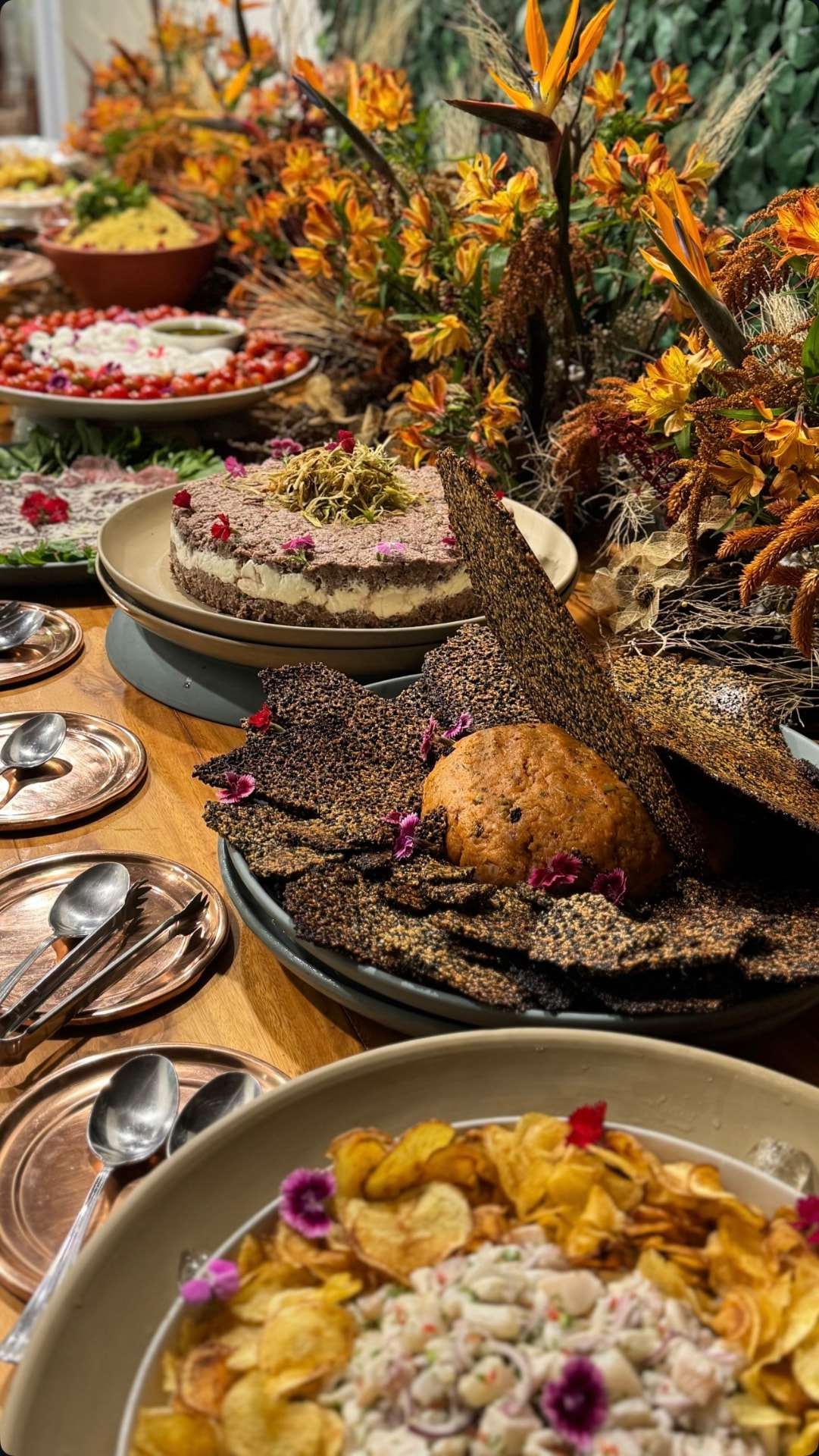 Mesa farta do Buffet Olimpo com entradas, ceviche, patês e flores alaranjadas